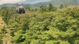 Eine Seilbahn schwebt über üppige grüne Wälder, während der majestätische Mount Fuji im Hintergrund sichtbar ist.