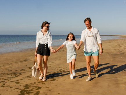 Eine Familie spaziert fröhlich am Strand entlang, während die Sonne am Himmel scheint und das Wasser sanft plätschert.