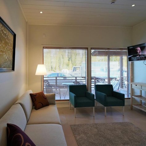 Ein gemütlicher Wohnbereich mit einem hellen Sofa, zwei grünen Sesseln und einem Fernseher an der Wand.