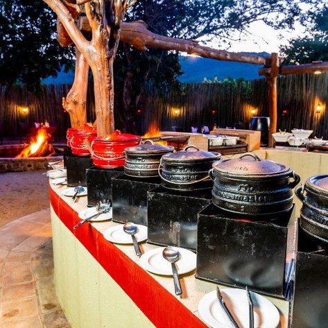 Ein rustikaler Essbereich im Freien mit mehreren Töpfen auf einem Tisch, umgeben von Bäumen und sanfter Beleuchtung.