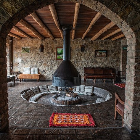 Ein gemütlicher Raum mit Steinwänden, einem zentralen Kamin und rustikalen Möbeln, die eine einladende Atmosphäre schaffen.