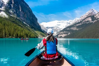 Eine Person paddelt in einem Kanu auf dem türkisfarbenen Wasser des Lake Louise, umgeben von majestätischen Bergen.