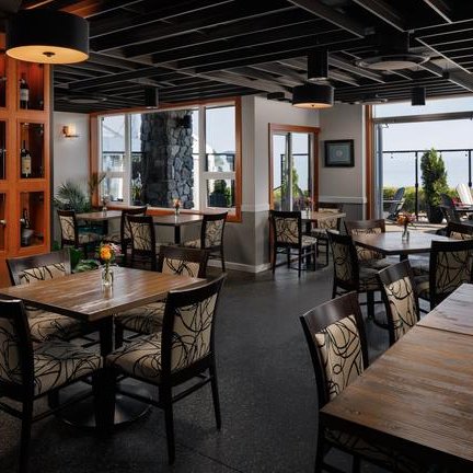 Ein elegantes Restaurant mit Holztischen und stilvollen Stühlen, das eine Aussicht auf den Strand bietet.