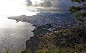 Ein atemberaubender Blick auf die Küste von Funchal, Madeira, mit dramatischen Wolken und sanften Hügeln im Hintergrund.