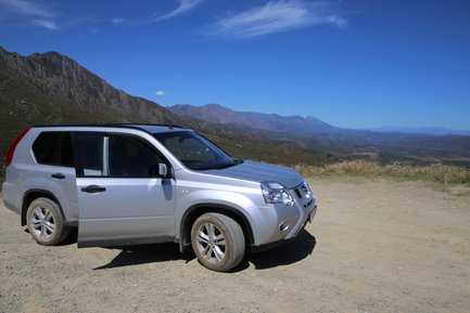 Ein geparktes Auto steht am Rand des Swartberg Passes mit Blick auf die weite Berglandschaft – Garden Route Familienreise