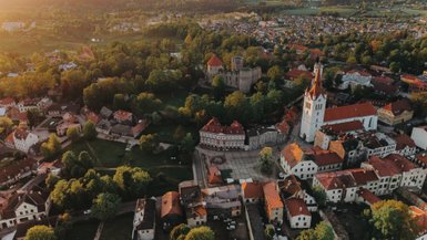 Eine malerische Stadtansicht mit historischen Gebäuden und einer Kirche, umgeben von üppigem Grün und sanften Hügeln.