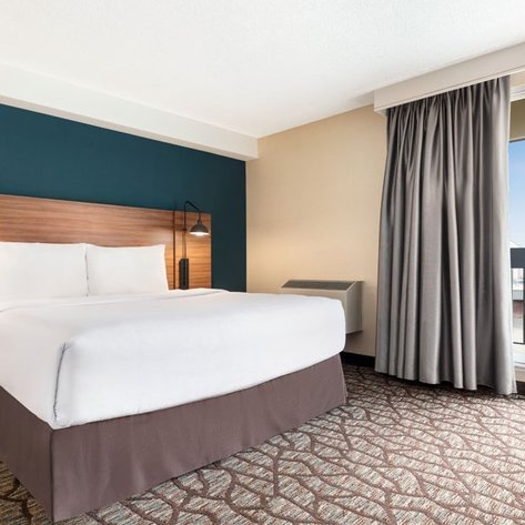 Ein modernes Hotelzimmer mit einem großen Bett, stilvollen Lampen und einem Fenster, das einen Blick auf die Stadt bietet.