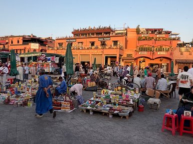 Lebendige Szenerie auf dem Djemaa el-Fnaa Platz in Marrakesch mit Ständen und Menschen in traditionellen Kleidern.