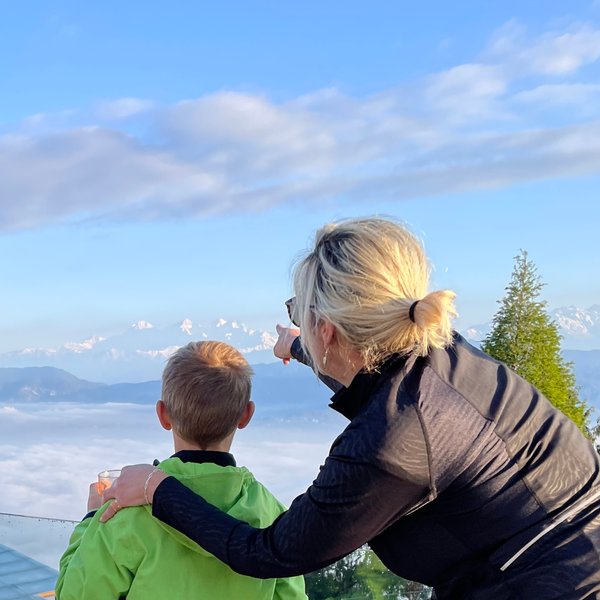 Eine Frau zeigt einem Jungen die majestätischen Himalaya-Berge, während sie über eine Wolkendecke blicken.