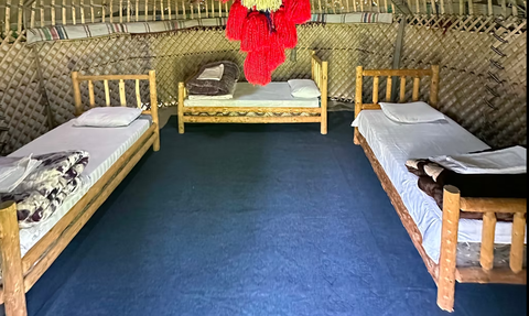 Ein traditionelles Jurteninnere mit drei Holzbetten, die mit weißen Laken und Kissen ausgestattet sind, auf einem blauen Teppich.