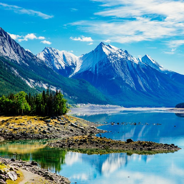 Ein klarer See spiegelt die majestätischen schneebedeckten Berge und den strahlend blauen Himmel wider.