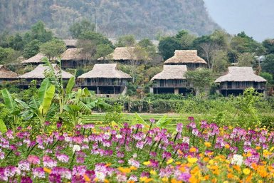 Bunte Blumenwiesen im Vordergrund, während traditionelle Hütten in der malerischen Landschaft im Hintergrund stehen.