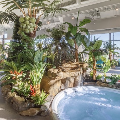 Ein luxuriöser Wellnessbereich mit einem Whirlpool, umgeben von üppigen Pflanzen und einem großen Fenster mit Blick auf die Natur.
