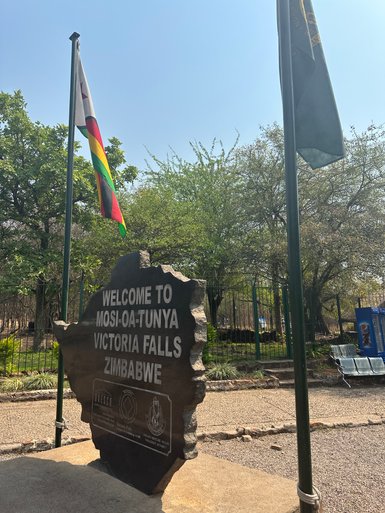 Ein markanter Stein mit der Aufschrift 'Willkommen in Mosi-oa-Tunya, Victoriafälle, Simbabwe' steht im Freien.