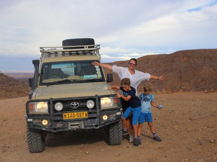 Eine Mutter steht mit ihren beiden Söhnen neben einem Jeep - Namibia Rundreise mit Kindern