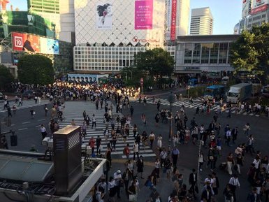 Eine große Menschenmenge überquert die belebte Shibuya-Kreuzung in Tokio, umgeben von modernen Gebäuden und Werbetafeln.