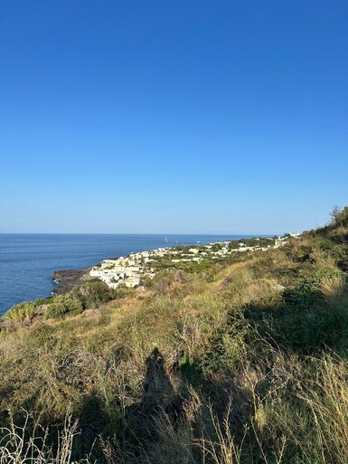 Eine malerische Küstenlandschaft mit weißen Häusern, die sanft am Hang liegen, umgeben von üppigem Grün und klarem Wasser.