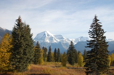 Ein majestätischer Berg mit schneebedecktem Gipfel erhebt sich über eine bunte Herbstlandschaft voller Bäume.