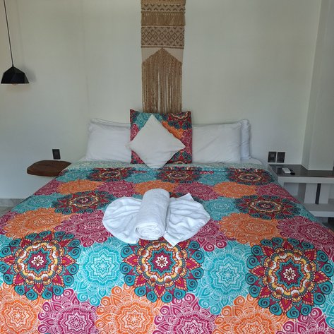 Ein farbenfrohes Bett mit einem bunten Bettbezug und einem gefalteten Handtuch auf der Decke in einem modernen Raum.