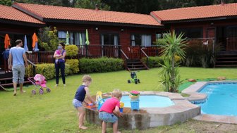 Zwei Kinder spielen am Rand eines kleinen Pools, während Erwachsene im Hintergrund entspannen und sich unterhalten.