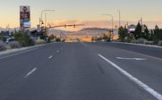 Eine breite Straße erstreckt sich unter einem sanften Sonnenuntergang, gesäumt von Geschäften und Verkehrssignalen.