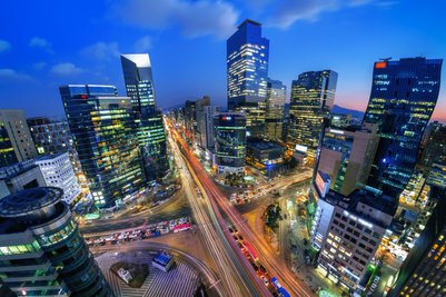 Die Stadt Seoul erstrahlt in der Dämmerung, mit leuchtenden Wolkenkratzern und lebhaften Straßen voller Autos.