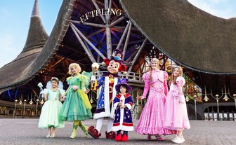 Eine Gruppe von fünf fröhlichen Charakteren in bunten Kostümen steht vor einem beeindruckenden Gebäude im Freizeitpark.
