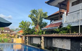 Ein glitzernder Pool spiegelt den blauen Himmel wider, umgeben von üppigem Grün und balinesischer Architektur.