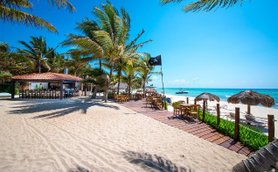 Ein sonniger Strand mit Palmen, einem Restaurant im Hintergrund und einem Boot, das sanft auf dem Wasser schaukelt.