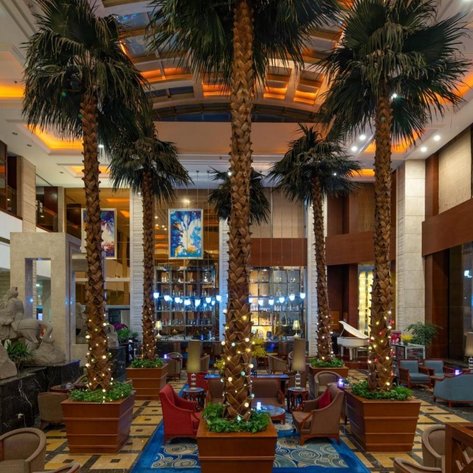 Im eleganten Hotel-Lobby stehen hohe Palmen, umgeben von stilvollen Sitzbereichen und sanfter Beleuchtung.