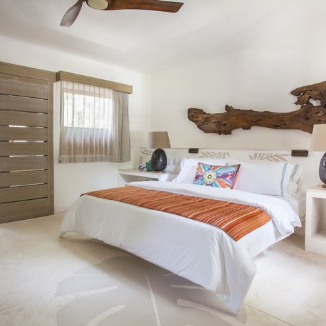 Ein helles Zimmer mit einem großen Bett, dekoriert mit einem bunten Kissen und einem rustikalen Holzstück an der Wand.