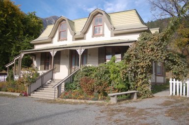 Ein charmantes, zweigeschossiges Haus mit einem gewellten Dach und bunten Blumen im Vordergrund, umgeben von üppigem Grün.