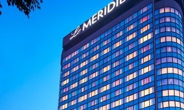 Das moderne Hotelgebäude Le Meridien strahlt in der Dämmerung mit leuchtenden Fenstern und einem klaren blauen Himmel.