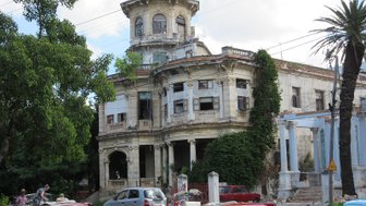 Ein verfallenes, historisches Gebäude mit einer beeindruckenden Fassade und verwilderten Pflanzen umgibt die Szenerie.