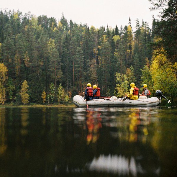 Eine Gruppe von fünf Personen in einem Schlauchboot auf einem ruhigen Fluss, umgeben von buntem Herbstlaub.