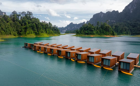 Eine Reihe von modernen, schwimmenden Bungalows liegt auf einem ruhigen, türkisfarbenen See, umgeben von üppiger Natur.