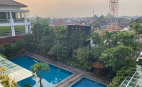 Ein Blick auf einen ruhigen Hotelpool, umgeben von üppigem Grün und Sonnenliegen, unter einem sanften Morgenhimmel.