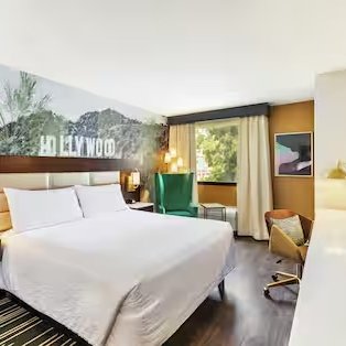 Ein modernes Hotelzimmer mit einem großen Bett und einem beeindruckenden Blick auf die Hollywood-Hügel im Hintergrund.