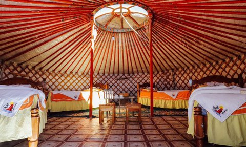 Ein traditionelles mongolisches Jurteninnere mit zwei Betten, bunten Decken und einem runden Dachfenster, das Licht hereinlässt.