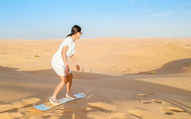 Teenager fährt Sandboard die Düne hinunter in der Wüste – Oman Reise mit Kindern