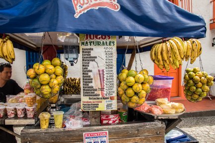 Ein Marktstand in Medellín bietet eine Vielzahl frischer Früchte und Säfte an, darunter Bananen und Orangen in Netzen.