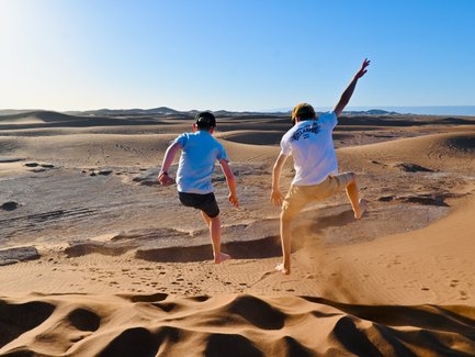 Kinder springen und haben Spaß auf den weiten Sanddünen der Sahara – Marokko Familienreise