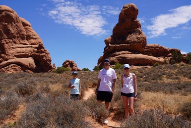Eine Familie steht in der Wüste von Moab, umgeben von beeindruckenden roten Felsen und strahlend blauem Himmel.