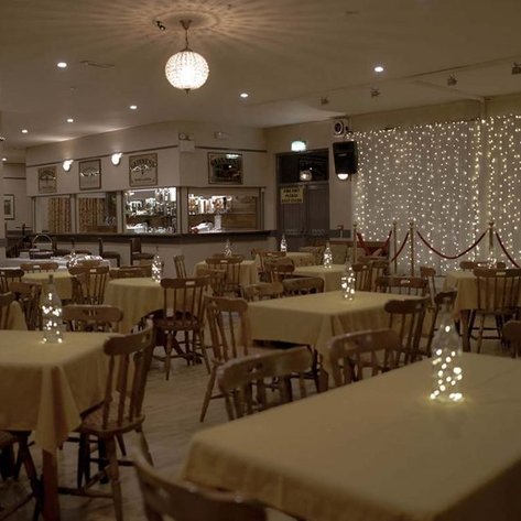 Ein gemütliches Restaurant mit runden Tischen, die mit gelben Tischdecken und dekorativen Lichtern geschmückt sind.