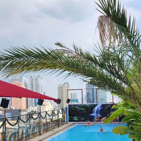 Ein lebhafter Rooftop-Pool mit Gästen, umgeben von Palmen und einer beeindruckenden Stadtansicht im Hintergrund.