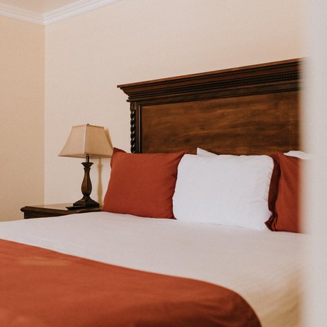 Ein gemütliches Schlafzimmer mit einem großen Bett, das mit roten und weißen Kissen dekoriert ist, und einer stilvollen Lampe.