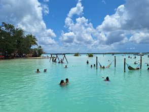 Eine Gruppe von Menschen schwimmt in einem türkisfarbenen Gewässer unter einem strahlend blauen Himmel mit weißen Wolken.