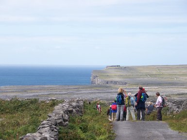 Eine Gruppe von Wanderern steht auf einem Weg und blickt auf die Küste mit steilen Klippen und dem weiten Ozean.