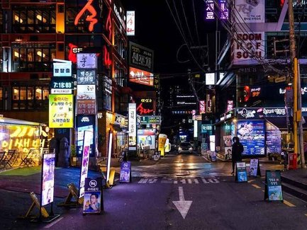 Eine belebte Straße in Gangnam, beleuchtet von bunten Neonlichtern und Werbetafeln, die das nächtliche Stadtleben zeigen.