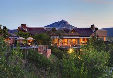 Eine malerische Lodge umgeben von üppigem Grün, mit einem beeindruckenden Berg im Hintergrund, der den Sonnenuntergang beleuchtet.